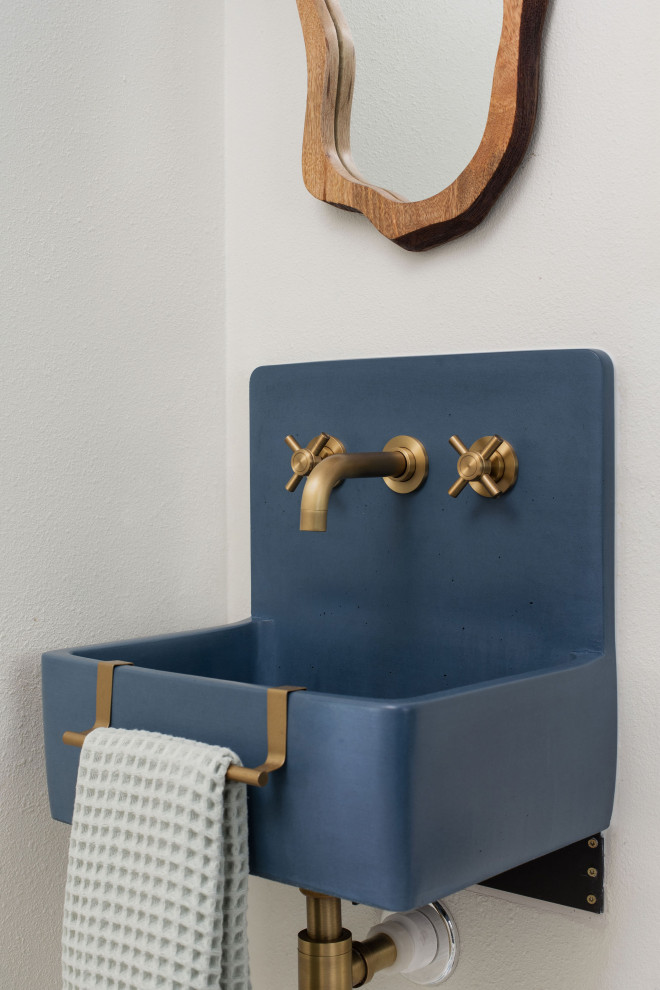 Bild på ett mellanstort blå blått toalett, med blå skåp, en toalettstol med separat cisternkåpa, blå kakel, vita väggar, cementgolv, ett väggmonterat handfat, bänkskiva i betong och blått golv