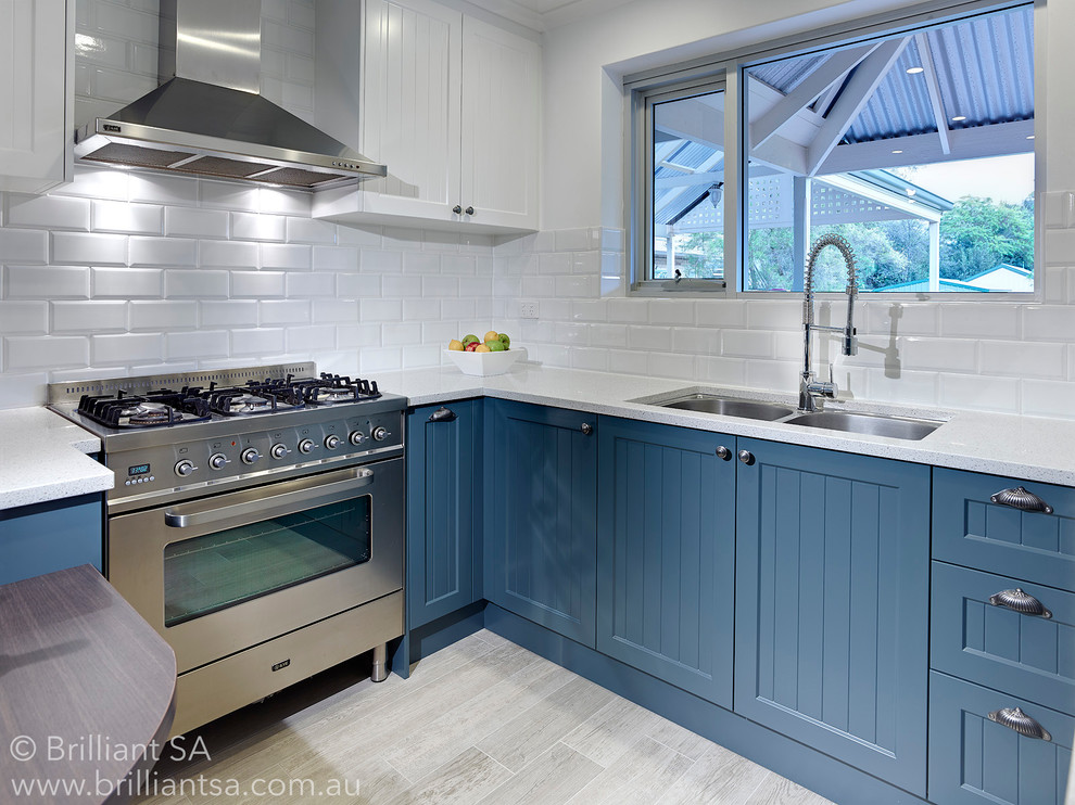This is an example of a beach style u-shaped eat-in kitchen in Adelaide with a drop-in sink, white cabinets, quartz benchtops, white splashback, porcelain splashback, white appliances and ceramic floors.
