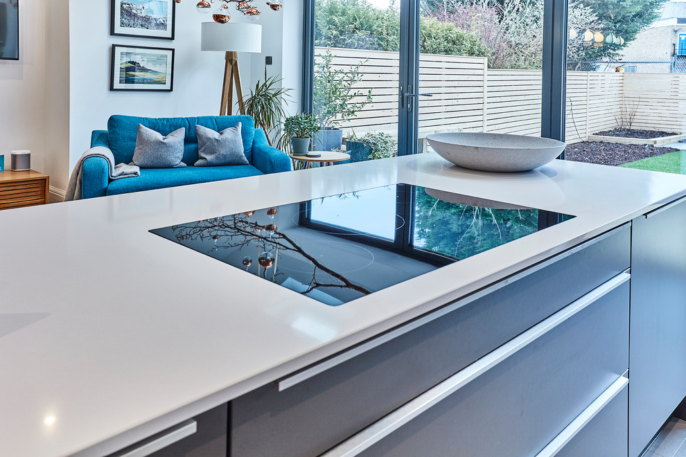 Inspiration for a mid-sized contemporary single-wall open plan kitchen in Other with flat-panel cabinets, grey cabinets, quartzite benchtops, metallic splashback, mirror splashback, stainless steel appliances, with island and white benchtop.