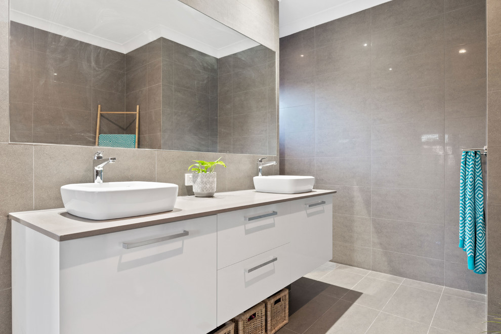 This is an example of a contemporary master bathroom in Perth with white cabinets, a freestanding tub, gray tile, ceramic tile, grey walls, ceramic floors, a vessel sink, solid surface benchtops, grey floor and grey benchtops.