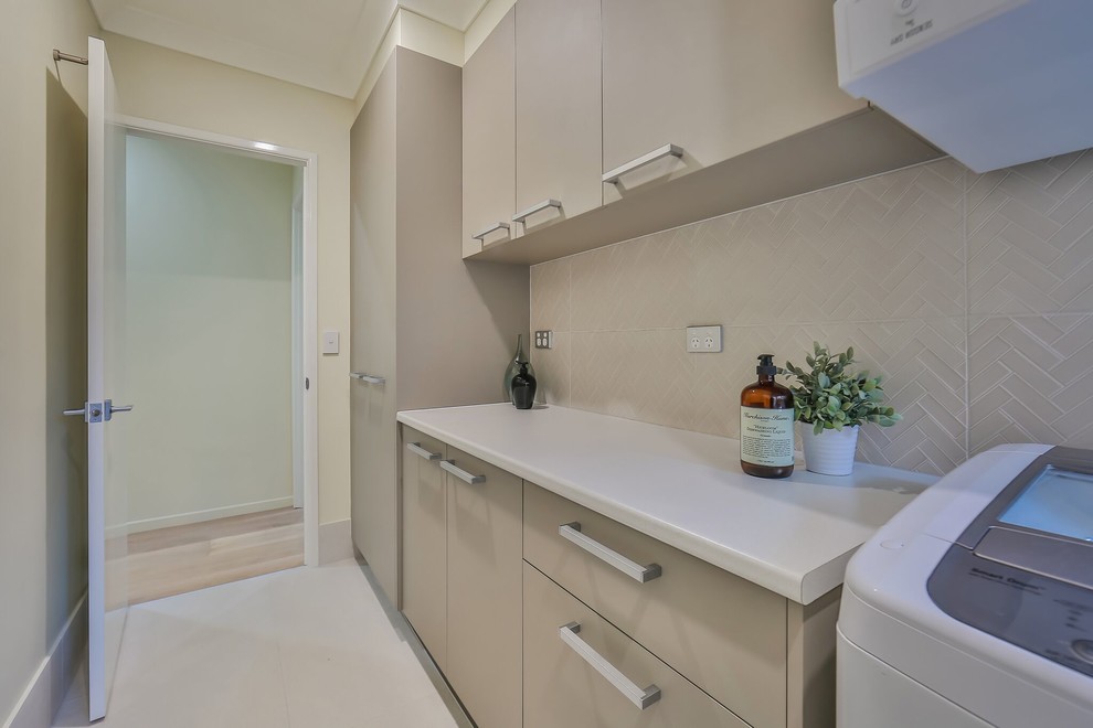 This is an example of a mid-sized contemporary galley dedicated laundry room in Brisbane with beige cabinets, laminate benchtops, beige walls, ceramic floors, beige floor and white benchtop.