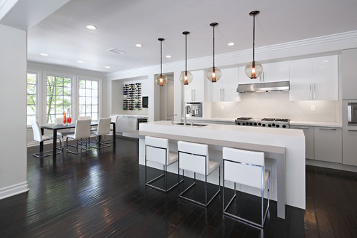 Modern open-plan kitchen with high-gloss white and gray RTA cabinets, long waterfall island with four stools, globe pendants, stainless range, and dark wood floors.