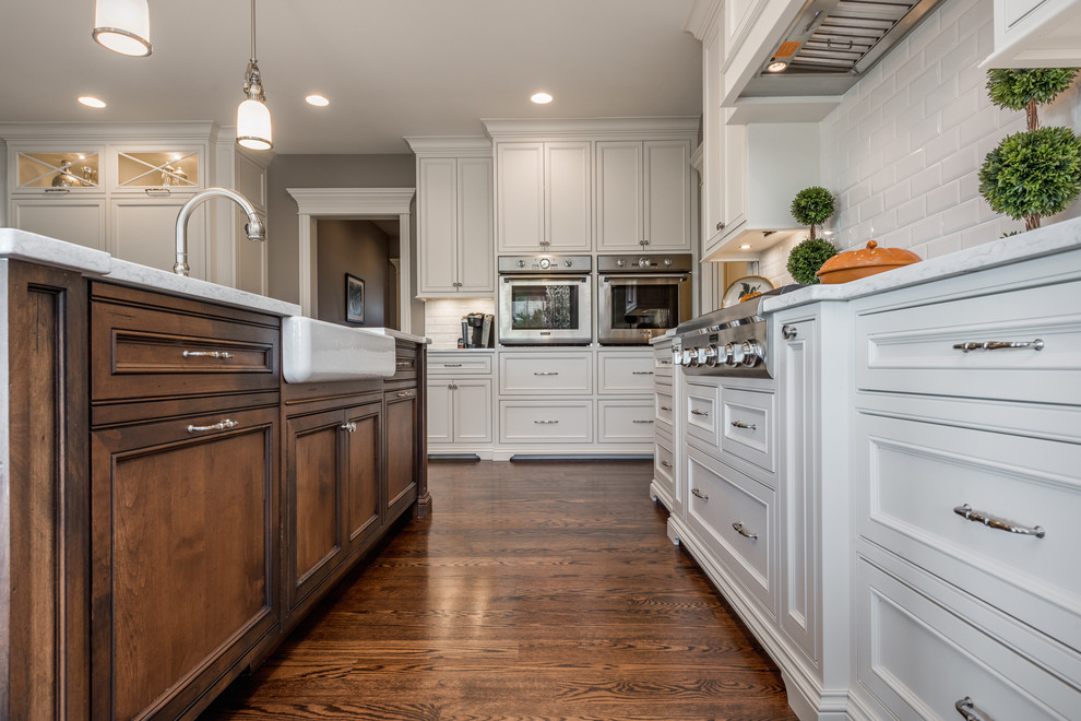 Design ideas for a large traditional u-shaped open plan kitchen in Chicago with a farmhouse sink, beaded inset cabinets, white cabinets, glass benchtops, white splashback, subway tile splashback, stainless steel appliances, dark hardwood floors, with island, brown floor and turquoise benchtop.