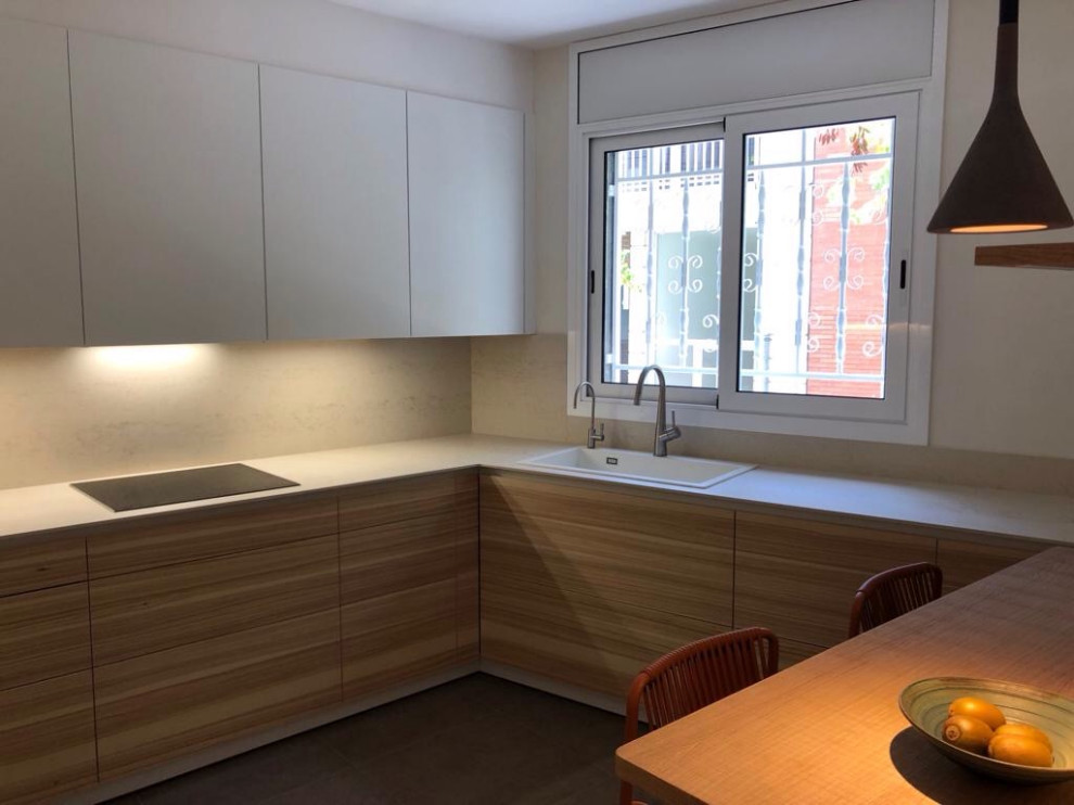Photo of a mid-sized contemporary l-shaped separate kitchen in Barcelona with a drop-in sink, recessed-panel cabinets, white cabinets, quartz benchtops, white splashback, black appliances, ceramic floors, no island, grey floor and white benchtop.