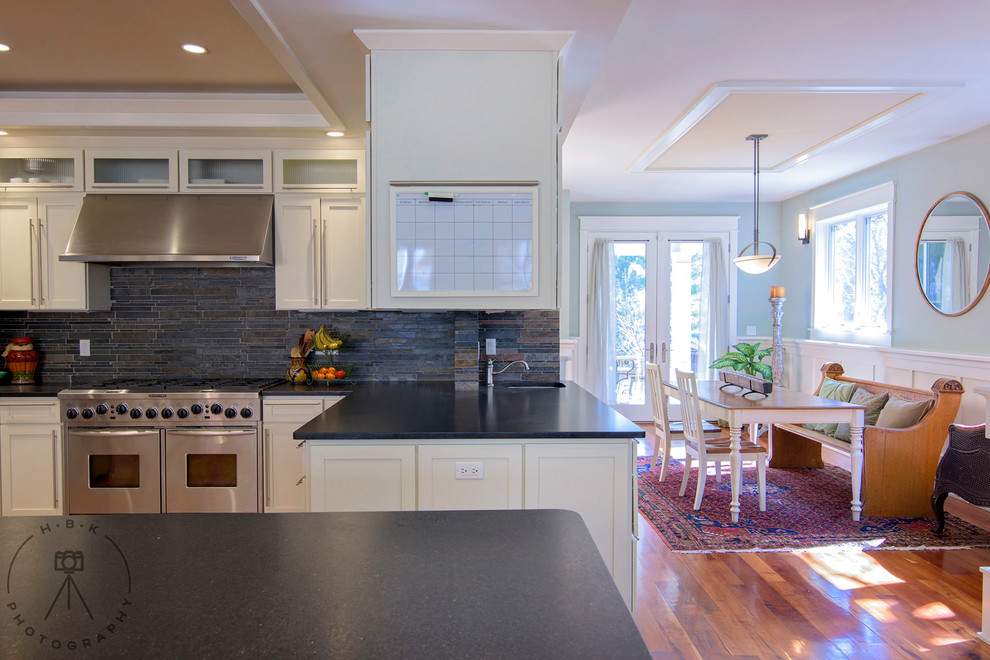 Inspiration for a large single-wall medium tone wood floor and brown floor open concept kitchen remodel with recessed-panel cabinets, white cabinets, black backsplash, stone tile backsplash, stainless steel appliances, an island and black countertops