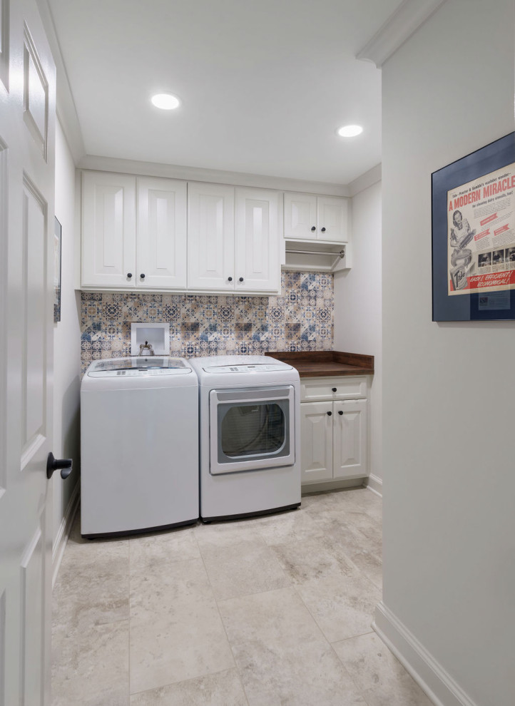 コロンバスにある高級な中くらいなビーチスタイルのおしゃれな洗濯室 (I型、レイズドパネル扉のキャビネット、白いキャビネット、ラミネートカウンター、マルチカラーのキッチンパネル、磁器タイルのキッチンパネル、白い壁、トラバーチンの床、左右配置の洗濯機・乾燥機、ベージュの床、茶色いキッチンカウンター) の写真