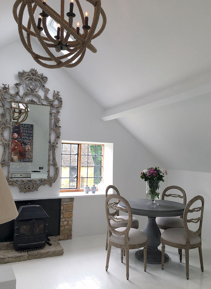 This is an example of a large transitional open plan dining in Gloucestershire with white walls, painted wood floors, a wood stove and a brick fireplace surround.