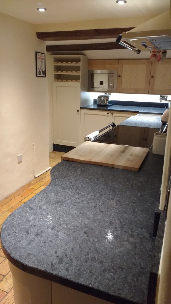 This is an example of a small eclectic l-shaped eat-in kitchen in Other with a farmhouse sink, shaker cabinets, granite benchtops, black splashback, stone slab splashback, coloured appliances, brick floors and no island.