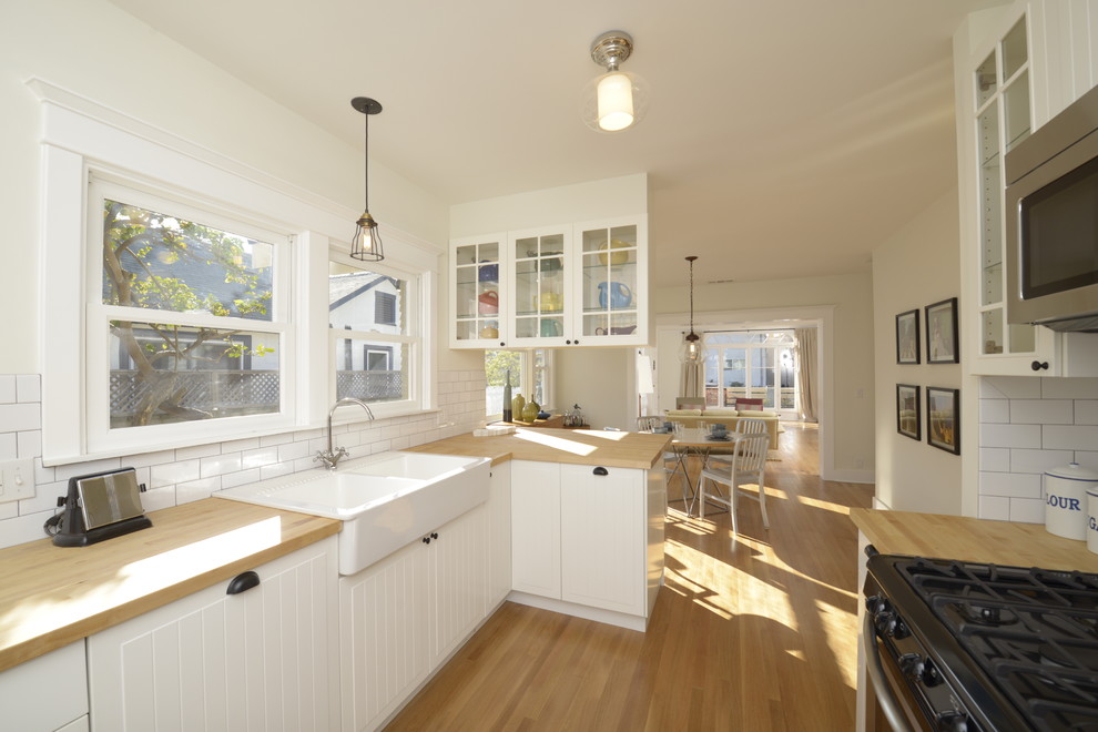 Inspiration for a mid-sized arts and crafts galley eat-in kitchen in Los Angeles with a peninsula, beaded inset cabinets, white cabinets, wood benchtops, white splashback, subway tile splashback, panelled appliances, a farmhouse sink and light hardwood floors.