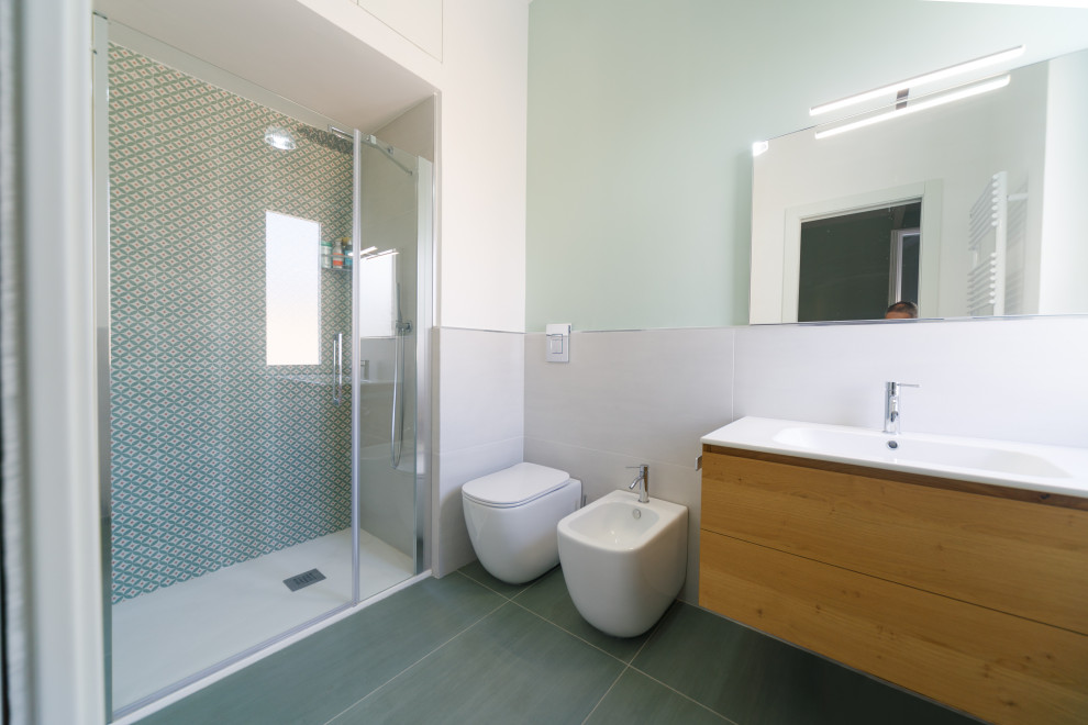 Bild på ett mellanstort funkis vit vitt badrum, med skåp i ljust trä, en toalettstol med separat cisternkåpa, grön kakel, porslinskakel, vita väggar, ett integrerad handfat, grönt golv och dusch med gångjärnsdörr