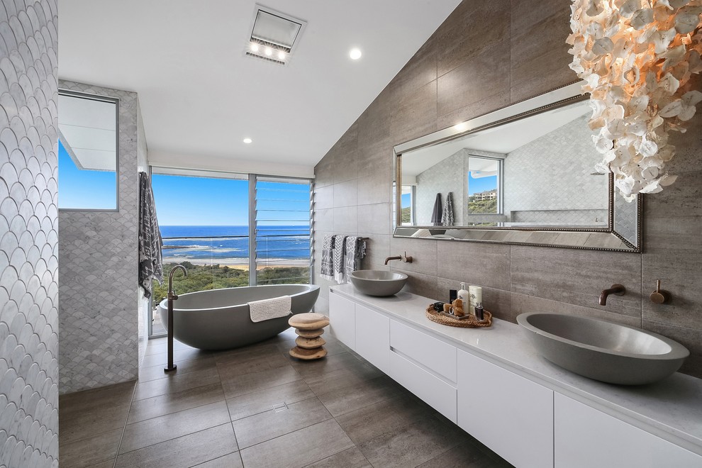 Design ideas for a tropical master bathroom in Central Coast with flat-panel cabinets, white cabinets, a freestanding tub, gray tile, a vessel sink and grey floor.