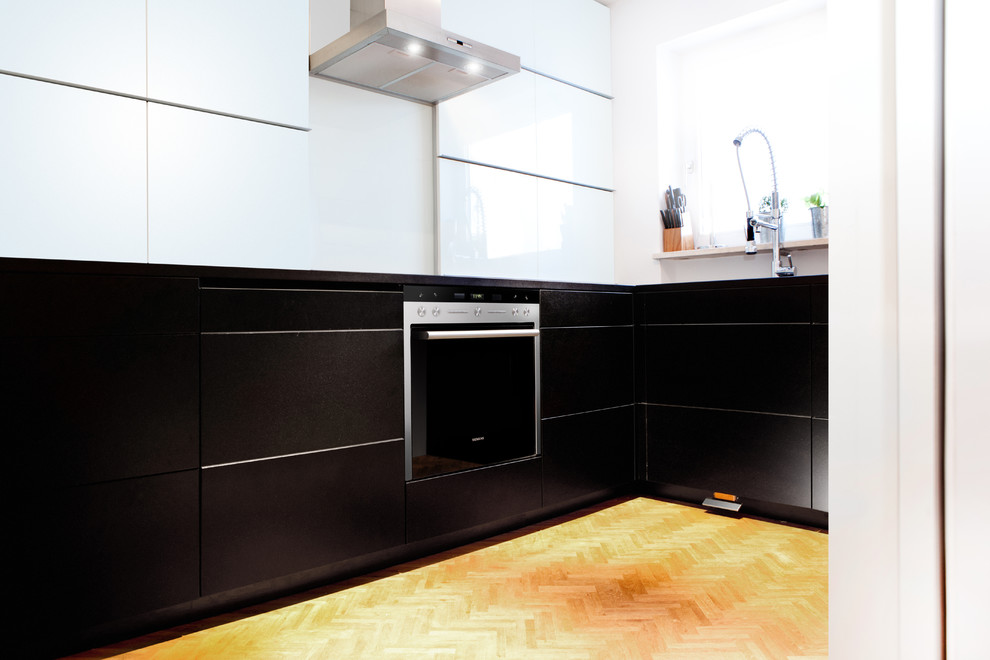 Inspiration for a large contemporary l-shaped open plan kitchen in Munich with an integrated sink, flat-panel cabinets, black cabinets, solid surface benchtops, black splashback, marble splashback, stainless steel appliances, medium hardwood floors, no island and brown floor.