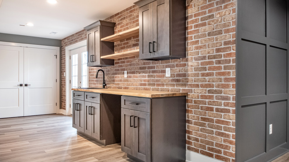 This is an example of a medium sized traditional single-wall wet bar in DC Metro with a submerged sink, shaker cabinets, wood worktops, red splashback, brick splashback, vinyl flooring, brown floors, brown worktops, feature lighting and grey cabinets.