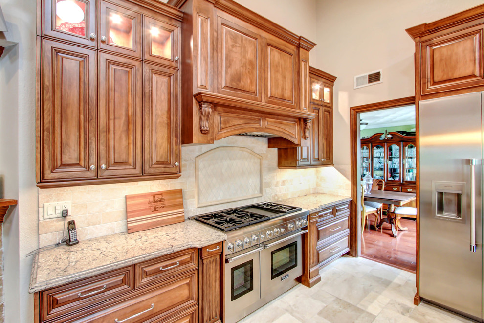 Photo of a large traditional l-shaped open plan kitchen in Los Angeles with an undermount sink, raised-panel cabinets, medium wood cabinets, quartz benchtops, beige splashback, travertine splashback, stainless steel appliances, porcelain floors, with island, white floor and beige benchtop.