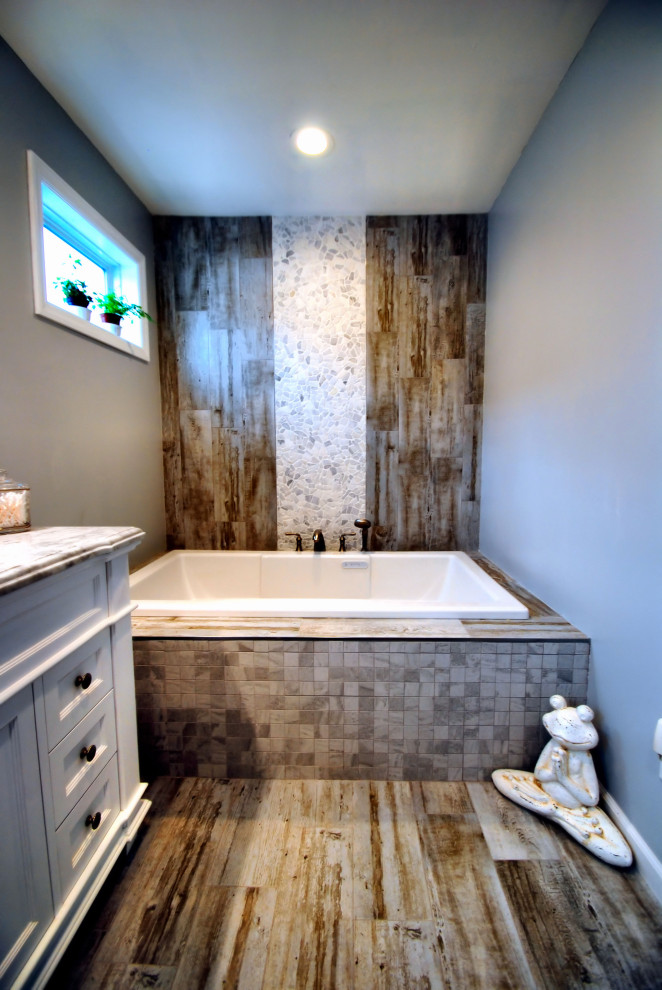 Photo of a mid-sized country master bathroom in New York with furniture-like cabinets, white cabinets, a drop-in tub, an alcove shower, a two-piece toilet, brown tile, pebble tile, grey walls, porcelain floors, an undermount sink, marble benchtops, brown floor, a sliding shower screen and multi-coloured benchtops.