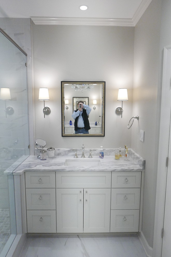 Example of a large transitional master white tile and porcelain tile porcelain tile and white floor freestanding bathtub design with shaker cabinets, white cabinets, a two-piece toilet, beige walls, an undermount sink, marble countertops, a hinged shower door and white countertops