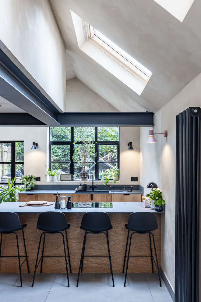 Mid-sized industrial eat-in kitchen in London with an integrated sink, flat-panel cabinets, medium wood cabinets, black appliances, ceramic floors, with island, grey floor, grey benchtop and exposed beam.