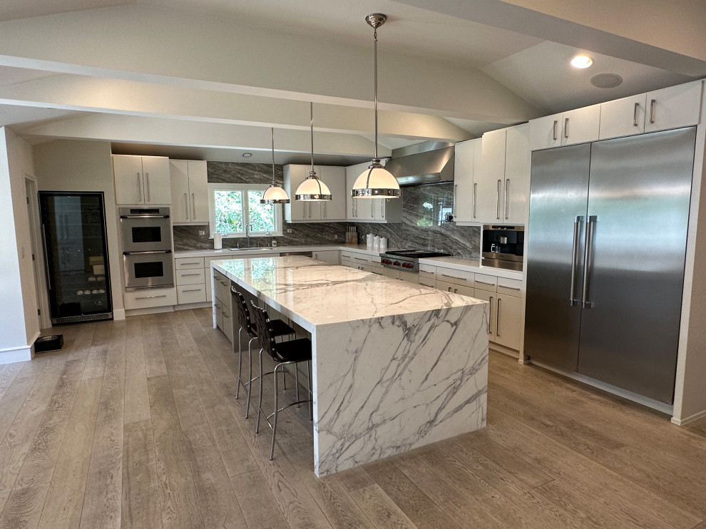 This is an example of a large contemporary l-shaped kitchen in San Francisco with an undermount sink, white cabinets, marble benchtops, grey splashback, porcelain splashback, stainless steel appliances, light hardwood floors, beige floor, white benchtop, flat-panel cabinets, with island and exposed beam.