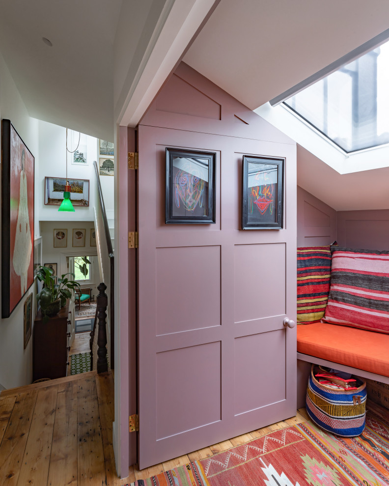 На фото: открытая гостиная комната среднего размера в стиле фьюжн с с книжными шкафами и полками, розовыми стенами, паркетным полом среднего тона, скрытым телевизором и панелями на части стены