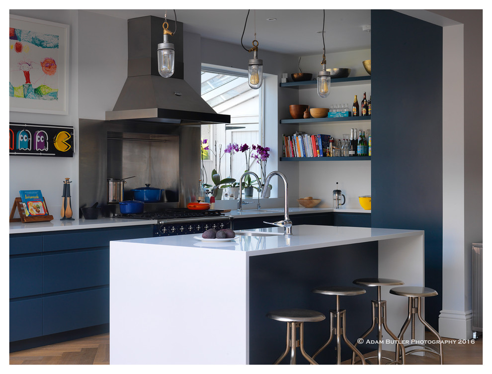 Inspiration for an industrial open plan kitchen in London with a single-bowl sink, flat-panel cabinets, blue cabinets, soapstone benchtops, stainless steel appliances, light hardwood floors and with island.
