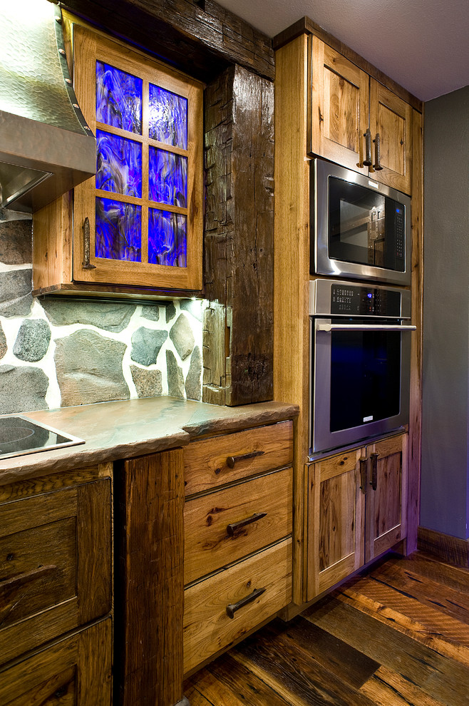 Mid-sized mountain style l-shaped medium tone wood floor eat-in kitchen photo with a farmhouse sink, shaker cabinets, distressed cabinets, concrete countertops, gray backsplash, stone slab backsplash, stainless steel appliances and an island