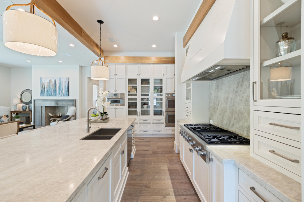 Enclosed kitchen - huge transitional u-shaped medium tone wood floor, brown floor and exposed beam enclosed kitchen idea in Houston with an integrated sink, beaded inset cabinets, white cabinets, quartz countertops, gray backsplash, stainless steel appliances, an island and beige countertops