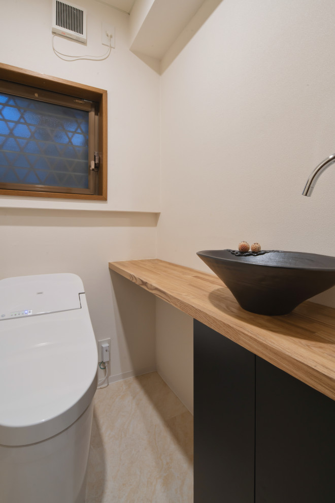 Nordisk inredning av ett litet brun brunt toalett, med möbel-liknande, skåp i ljust trä, en toalettstol med hel cisternkåpa, vinylgolv, träbänkskiva och beiget golv