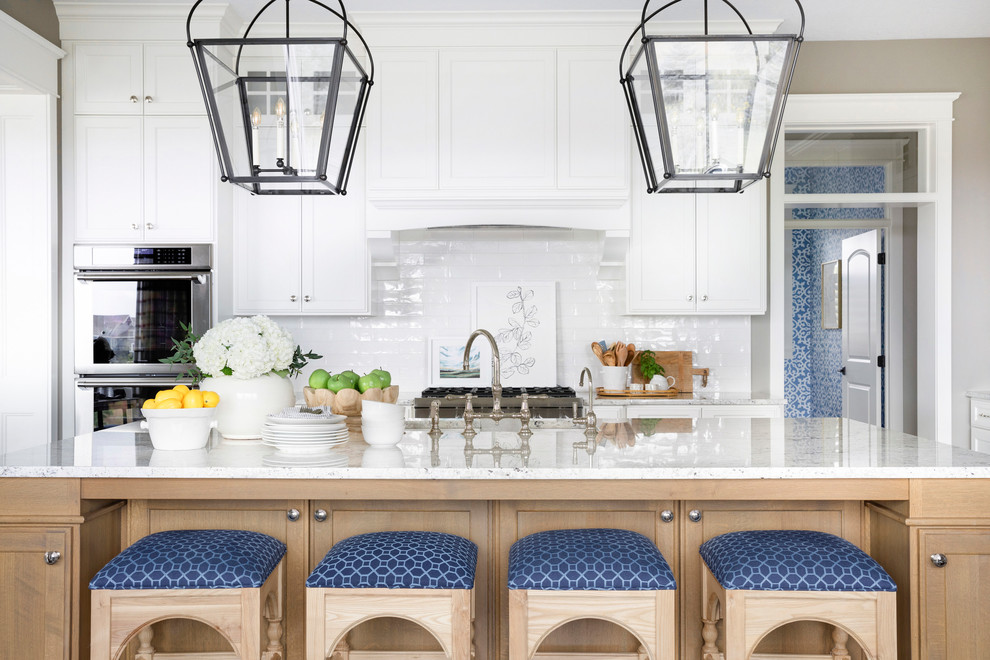 Photo of a beach style kitchen in Minneapolis with recessed-panel cabinets, white cabinets, white splashback, subway tile splashback, stainless steel appliances and with island.