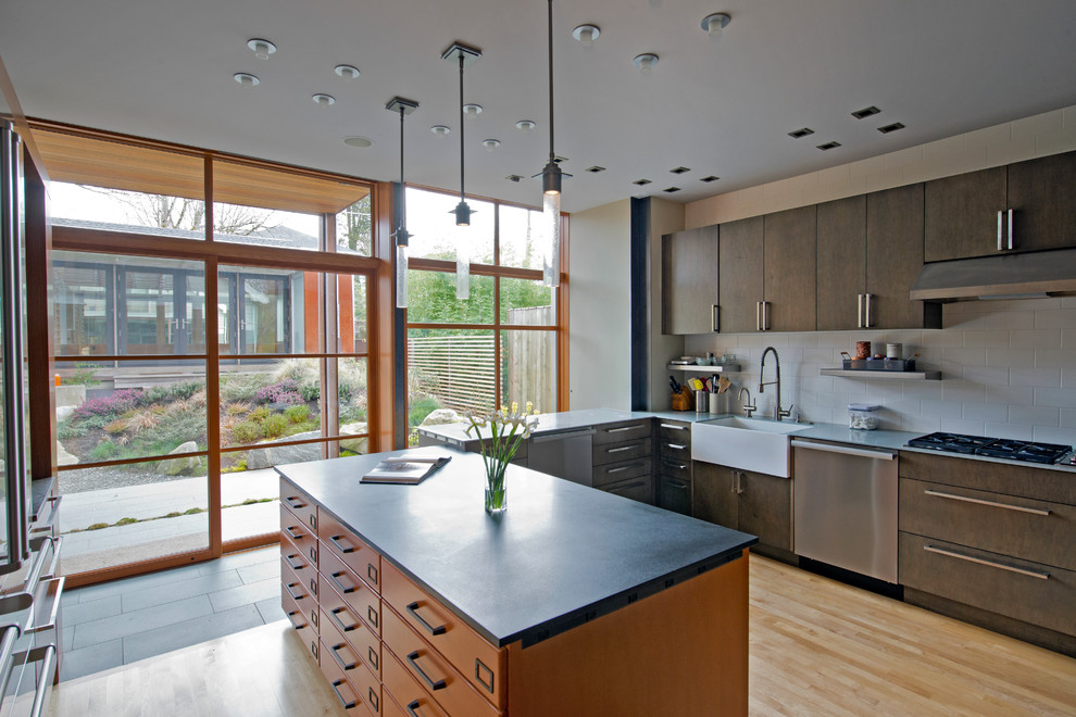 This is an example of a mid-sized modern u-shaped separate kitchen in Seattle with a farmhouse sink, flat-panel cabinets, medium wood cabinets, white splashback, stainless steel appliances, light hardwood floors, with island and subway tile splashback.