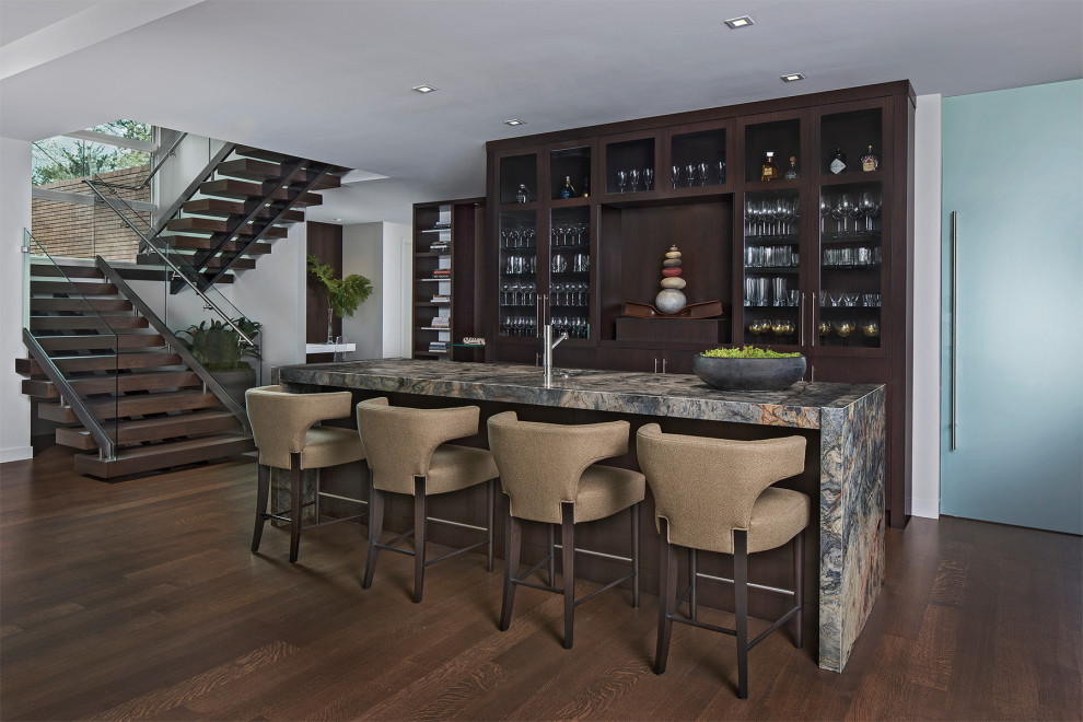 Photo of a contemporary galley home bar in Detroit with glass-front cabinets, dark wood cabinets, dark hardwood floors, brown floor and grey benchtop.