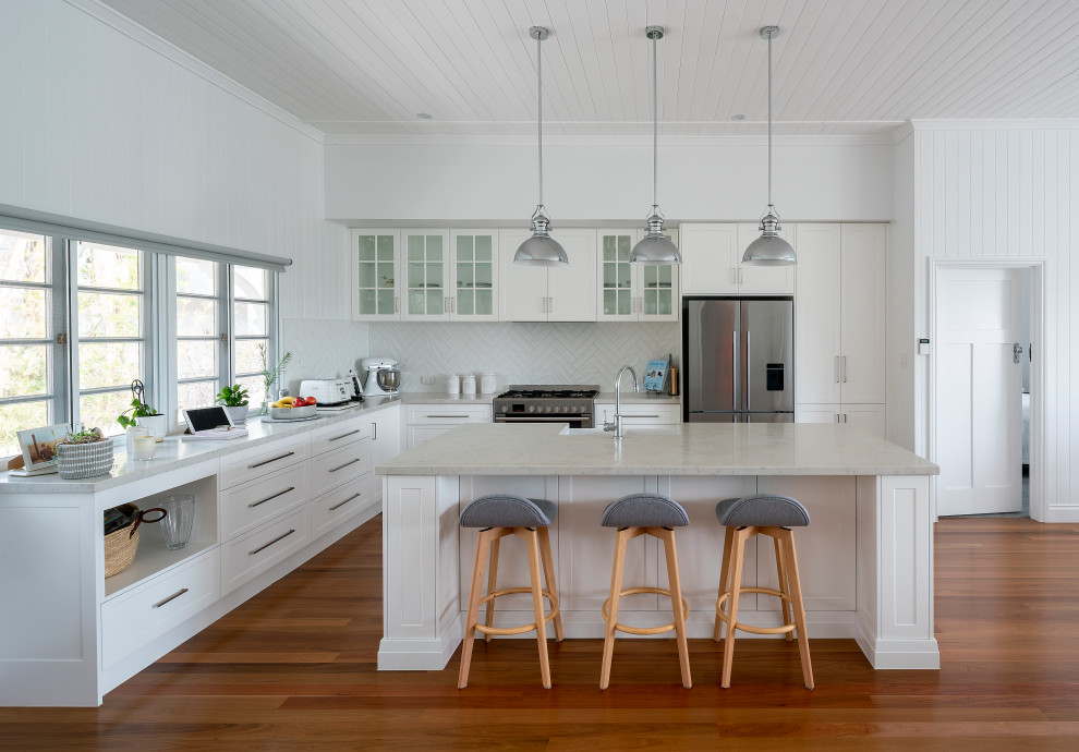 Design ideas for a nautical l-shaped kitchen in Brisbane with a belfast sink, shaker cabinets, white cabinets, white splashback, stainless steel appliances, medium hardwood flooring, an island, brown floors, grey worktops and a timber clad ceiling.