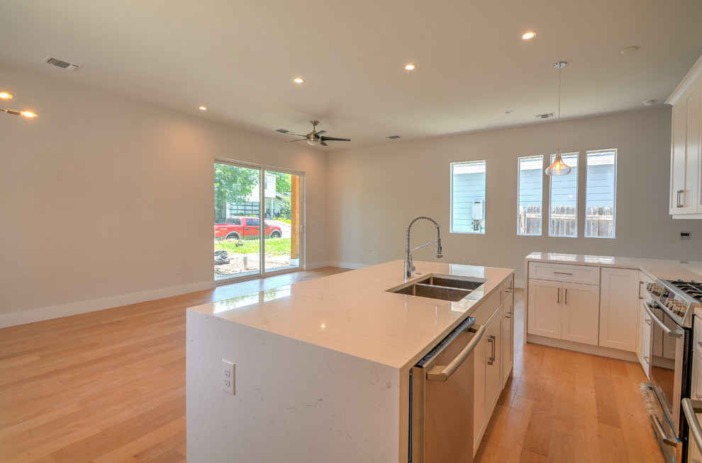 Inspiration for a mid-sized transitional single-wall medium tone wood floor and brown floor open concept kitchen remodel in Austin with a double-bowl sink, shaker cabinets, white cabinets, marble countertops, gray backsplash, stone tile backsplash, stainless steel appliances, an island and white countertops