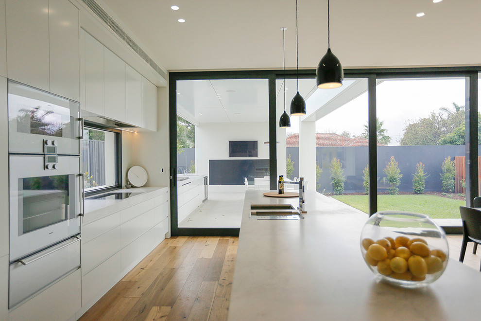 Inspiration for a mid-sized contemporary single-wall eat-in kitchen in Melbourne with flat-panel cabinets, white cabinets, with island, a double-bowl sink, marble benchtops, window splashback, stainless steel appliances and medium hardwood floors.