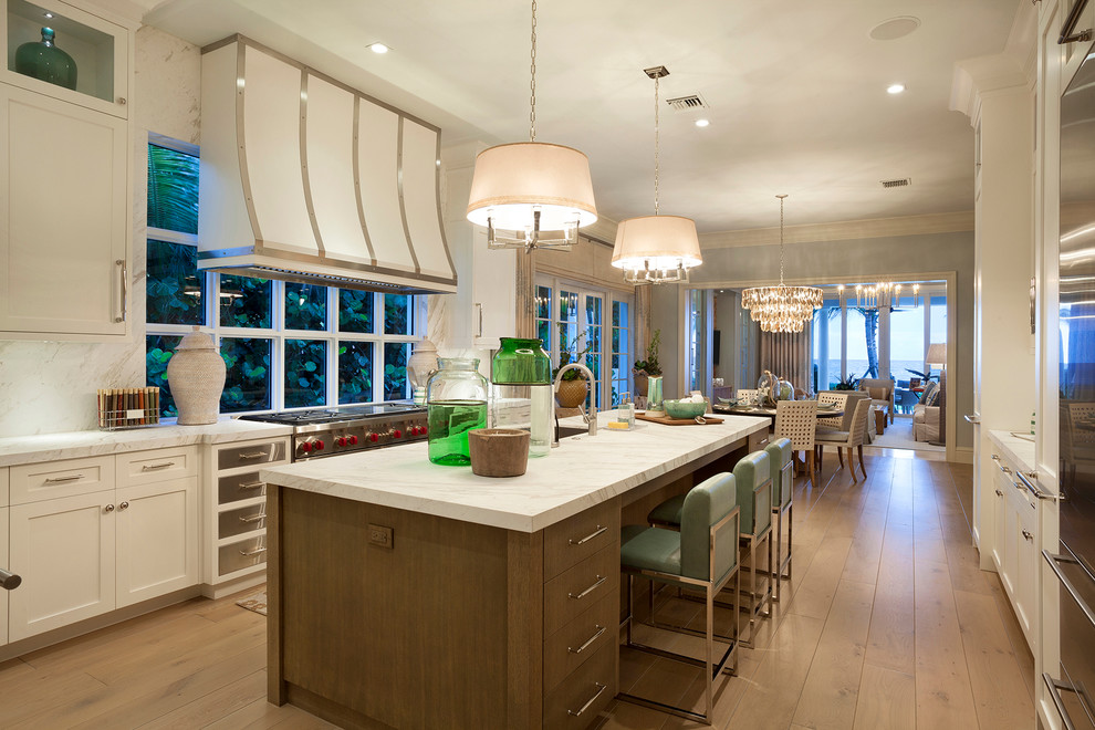 Expansive transitional l-shaped open plan kitchen in Miami with shaker cabinets, white cabinets, marble benchtops, white splashback, stainless steel appliances, light hardwood floors and with island.