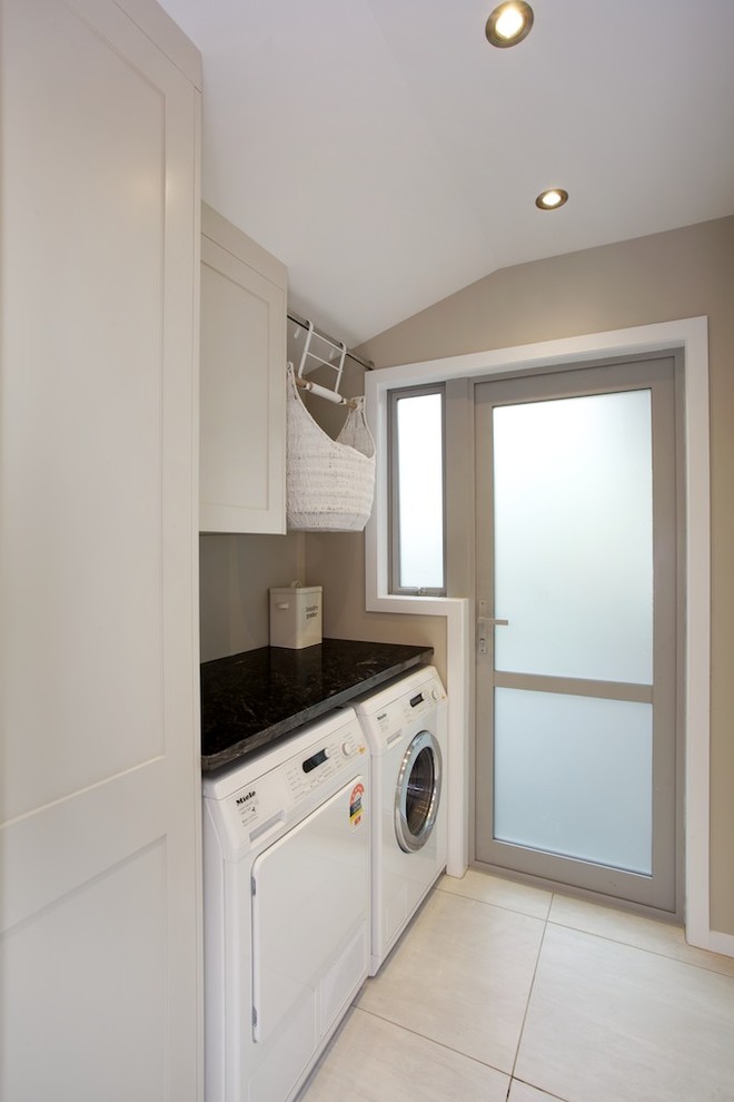 This is an example of a large contemporary u-shaped laundry room in Auckland with recessed-panel cabinets, white cabinets, granite benchtops, brown splashback, mosaic tile splashback and ceramic floors.