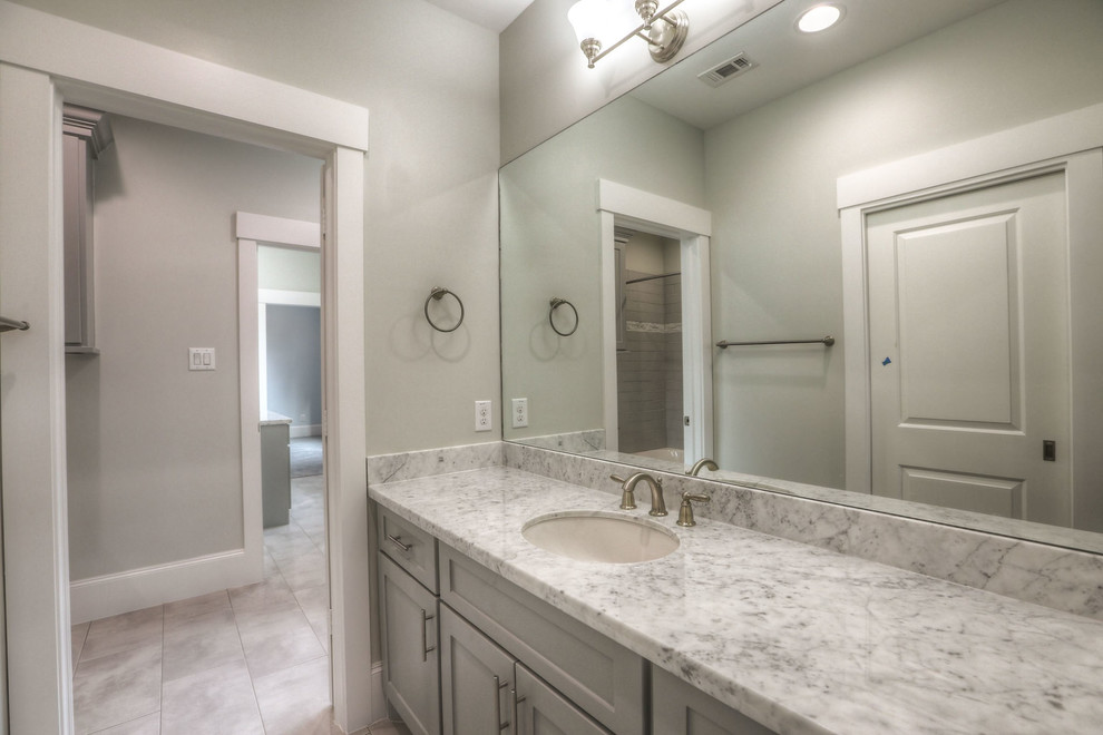Design ideas for a mid-sized transitional 3/4 bathroom in Houston with shaker cabinets, grey cabinets, an alcove shower, a two-piece toilet, beige tile, porcelain tile, beige walls, porcelain floors, an undermount sink, marble benchtops, beige floor and a hinged shower door.