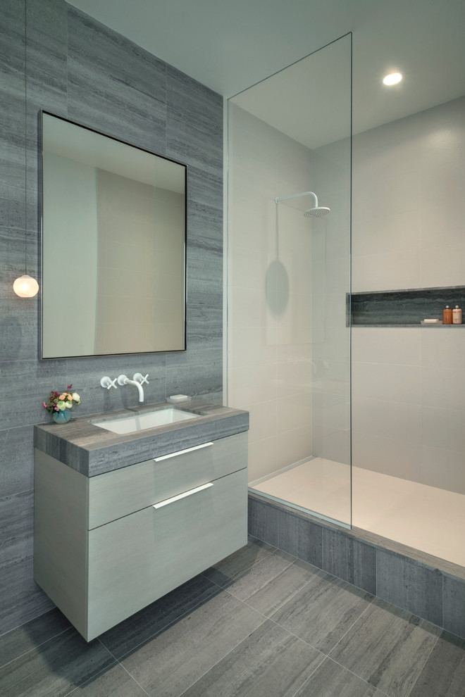 Photo of a mid-sized modern kids bathroom in New York with flat-panel cabinets, light wood cabinets, an open shower, a wall-mount toilet, gray tile, stone tile, white walls, marble floors, an undermount sink and marble benchtops.