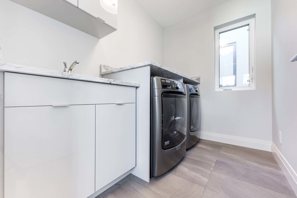 Inspiration for a mid-sized contemporary single-wall utility room in Edmonton with an undermount sink, flat-panel cabinets, white cabinets, white walls and a side-by-side washer and dryer.