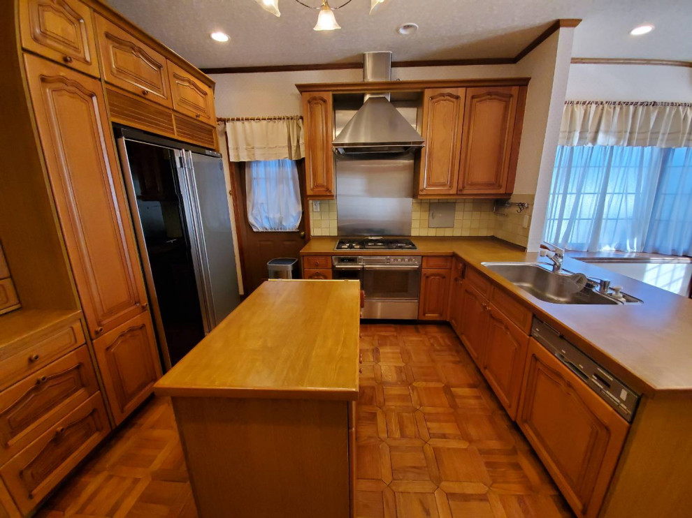 This is an example of a mid-sized country l-shaped eat-in kitchen in Nagoya with an undermount sink, beaded inset cabinets, medium wood cabinets, wood benchtops, yellow splashback, cement tile splashback, stainless steel appliances, plywood floors, brown floor and brown benchtop.