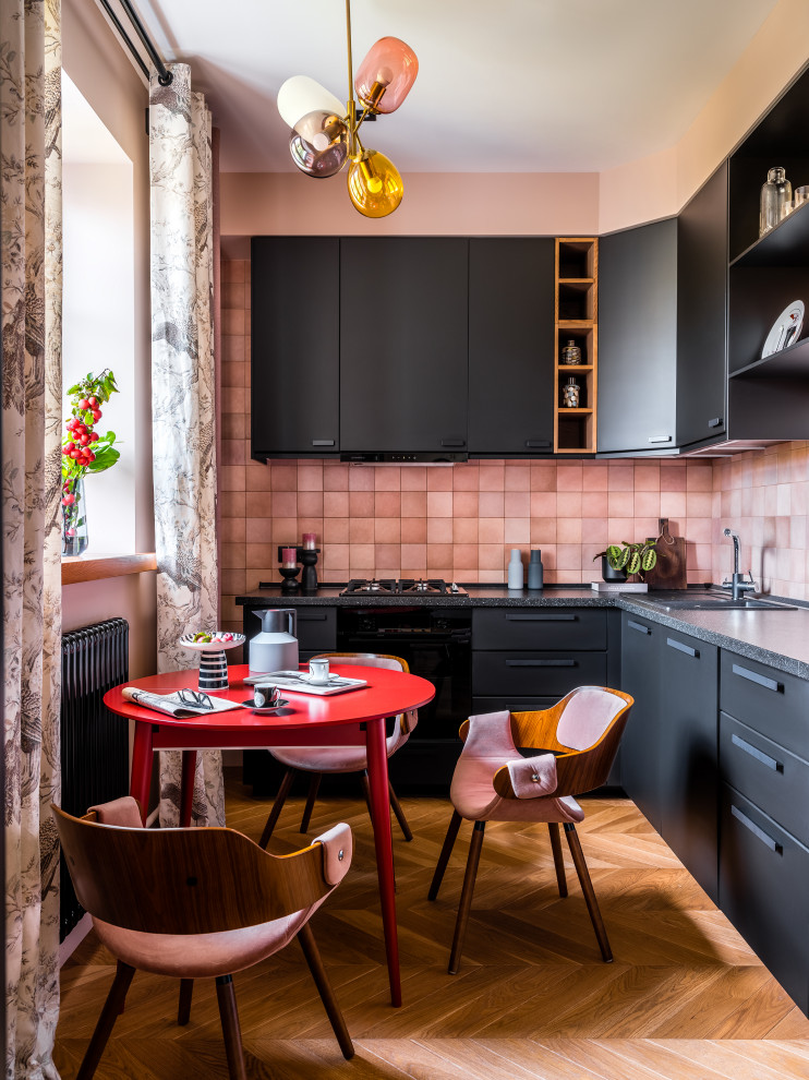 Photo of a mid-sized transitional l-shaped separate kitchen in Moscow with a drop-in sink, flat-panel cabinets, black cabinets, solid surface benchtops, pink splashback, ceramic splashback, black appliances, medium hardwood floors, no island and black benchtop.
