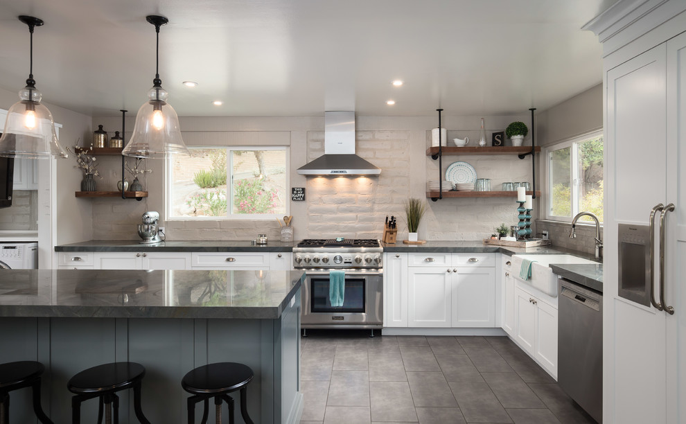 Mid-sized country l-shaped kitchen in San Francisco with a farmhouse sink, white cabinets, granite benchtops, grey splashback, brick splashback, stainless steel appliances, cement tiles, with island, grey floor and grey benchtop.