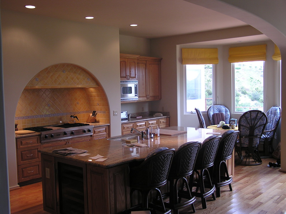 This is an example of a mid-sized mediterranean l-shaped kitchen in Los Angeles with a double-bowl sink, raised-panel cabinets, medium wood cabinets, yellow splashback, ceramic splashback, stainless steel appliances, medium hardwood floors and with island.