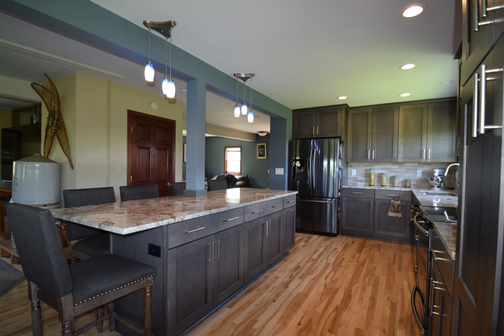 Inspiration for a transitional l-shaped light wood floor eat-in kitchen remodel with an undermount sink, shaker cabinets, gray cabinets, granite countertops, multicolored backsplash, stone tile backsplash, stainless steel appliances, an island and multicolored countertops