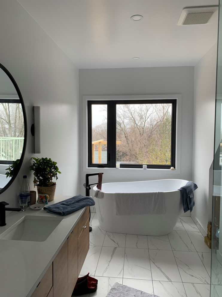This is an example of a mid-sized contemporary 3/4 bathroom in Toronto with flat-panel cabinets, light wood cabinets, a freestanding tub, a corner shower, white walls, marble floors, an undermount sink, white floor, a hinged shower door, white benchtops, a single vanity and a floating vanity.