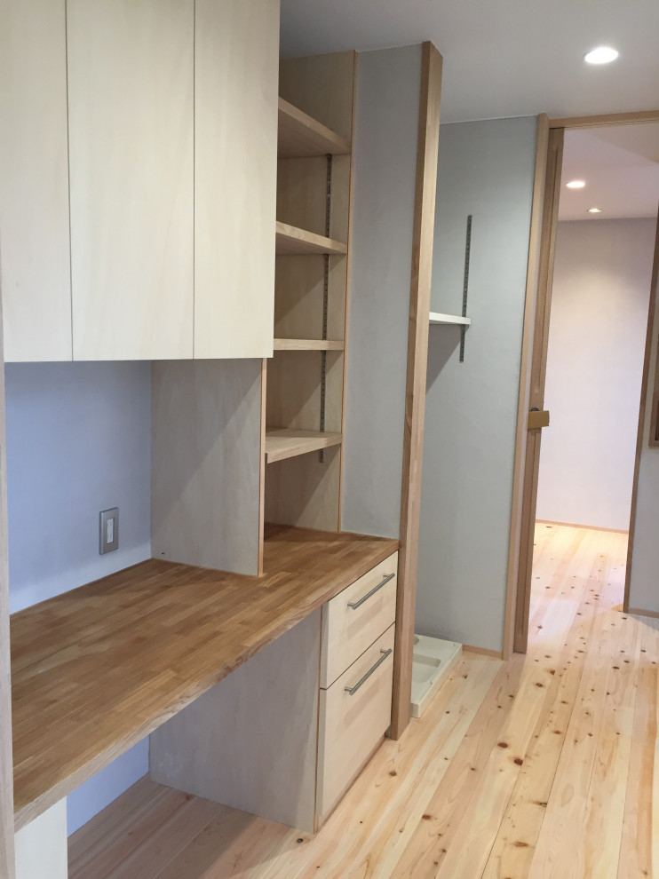Mid-sized scandinavian single-wall utility room in Other with wood benchtops, white walls, light hardwood floors, a stacked washer and dryer, beige benchtop and wallpaper.