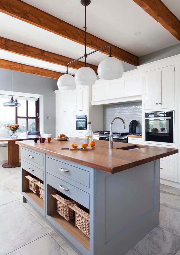 This is an example of a transitional galley eat-in kitchen in Other with an undermount sink, shaker cabinets, white cabinets, wood benchtops, grey splashback, stainless steel appliances and with island.
