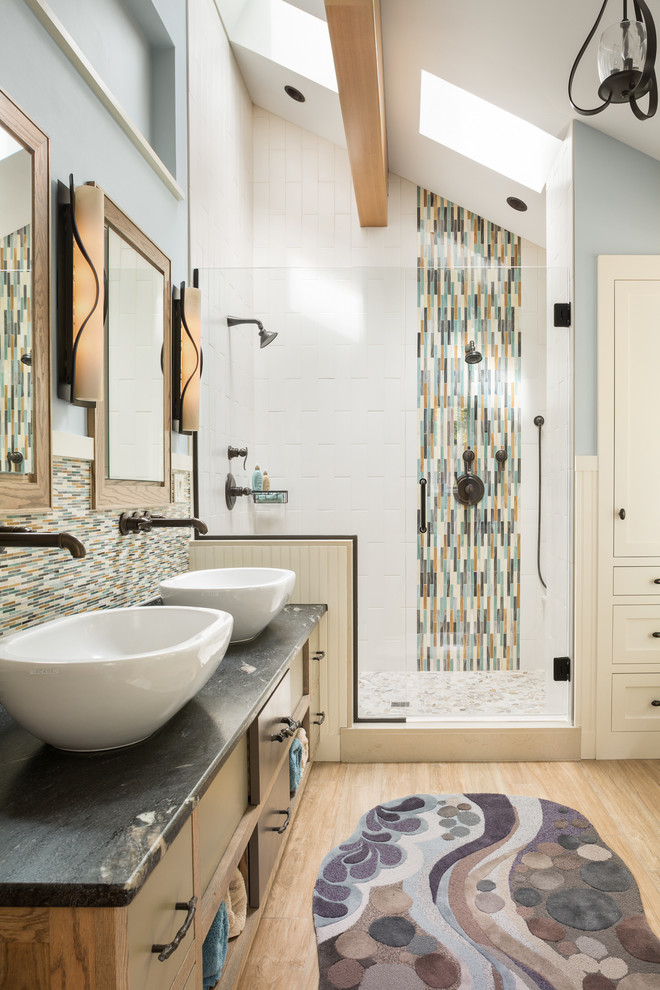 Design ideas for a mid-sized contemporary master bathroom in Portland Maine with medium wood cabinets, a freestanding tub, an alcove shower, blue walls, light hardwood floors, a vessel sink, granite benchtops, flat-panel cabinets, multi-coloured tile, matchstick tile, brown floor, a hinged shower door and black benchtops.