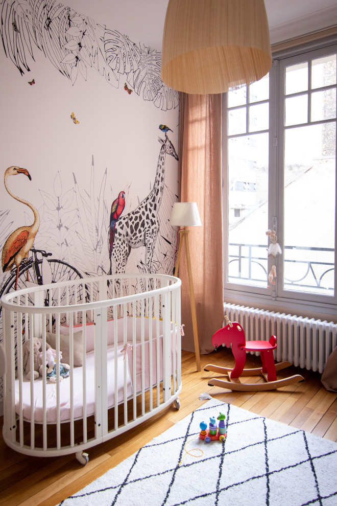 Photo of a mid-sized contemporary nursery for girls in Paris with beige walls, light hardwood floors, brown floor and wallpaper.