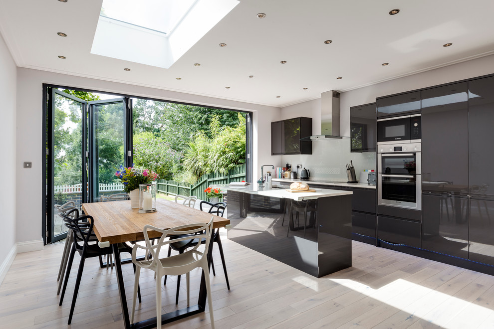 Photo of a contemporary eat-in kitchen in London with an undermount sink, flat-panel cabinets, black cabinets, light hardwood floors and with island.