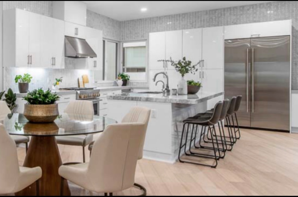 Medium sized traditional u-shaped open plan kitchen in Los Angeles with a single-bowl sink, flat-panel cabinets, white cabinets, marble worktops, grey splashback, marble splashback, stainless steel appliances, light hardwood flooring, an island and grey worktops.